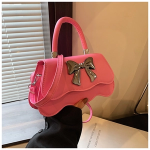 Detail of pink crossbody bag with large silver metal bow and stylish curved edge
