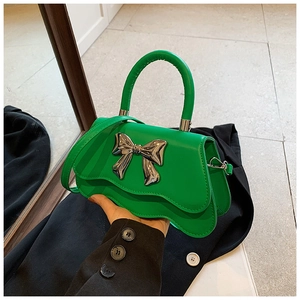 Detail of bright green leather handbag with silver metallic bow and wavy edge design