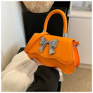Detail of orange handbag with silver metal bow accent and wavy bottom edge design