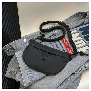 Close-up of black crescent crossbody bag with braided rope strap on denim jacket