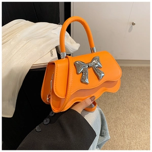 Detail of orange handbag with silver bow, wavy bottom design and round handle