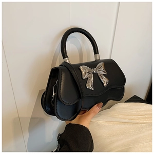 Detail of black leather handbag featuring a large silver metallic bow and wavy edge