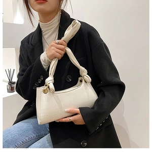 Detail of crocodile embossed cream white underarm bag featuring a knotted shoulder strap style