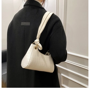 Close-up of a cream faux crocodile skin underarm bag with unique knotted strap detail