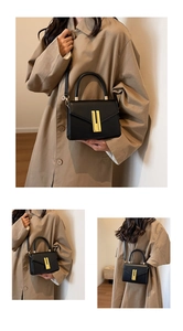 Macro detail of black lychee leather crossbody bag with golden metal buckle and top handle