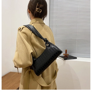 Detail of black crocodile pattern shoulder bag with a unique strap knot and gold hardware