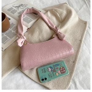 Pink crocodile pattern shoulder bag with a soft knot handle detail in a cozy setting