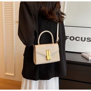Detail of cream leather square crossbody bag with gold metal clasp on a stylish model