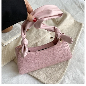 Detailed close-up of pink crocodile pattern texture and satin knotted handle of the handbag