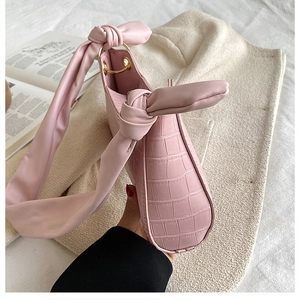 Detailed close-up of pink faux crocodile skin texture and knotted wide bow strap