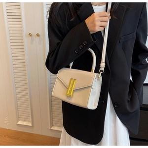 Chic cream crossbody bag with gold lock detail worn by model in black suit