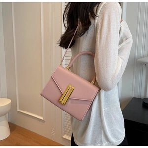 Detail of pink leather handbag with gold H-clasp being carried by a model
