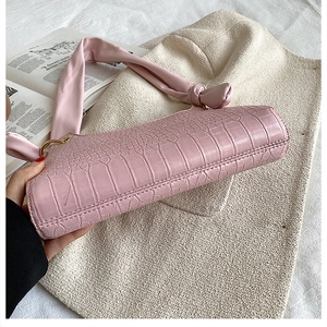 Detail of light pink crocodile pattern handbag with unique ruched leather shoulder strap