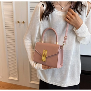 Pink crossbody bag with gold lock detail worn by model in a minimalist interior setting
