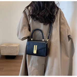 Detail of black textured leather crossbody bag with dual gold clasps on a beige trench coat