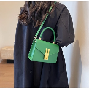 Detail view of emerald green leather crossbody bag with elegant gold metal bar lock closure