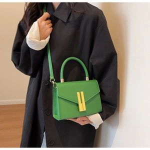 Side view of a green lychee leather handbag with a gold buckle on a black coat outfit