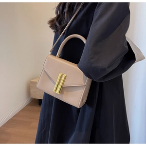 Detail of minimalist beige leather handbag with dual gold metal clasps on black dress