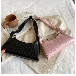Detail view of crocodile pattern baguette bags in black and pink with knotted strap