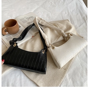 Detail of crocodile pattern baguette bags in black and cream with knotted straps