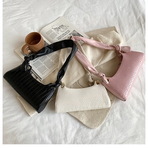 Detailed view of crocodile pattern shoulder bags in black, white and pink on soft bedding