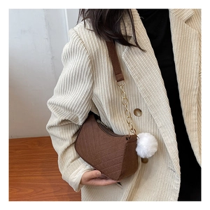 Detalle de bolso bandolera marrón acolchado con cadena dorada y pompón blanco de adorno