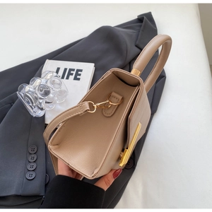 Detailed close-up of beige lychee grain leather handbag with gold metal lock and handle