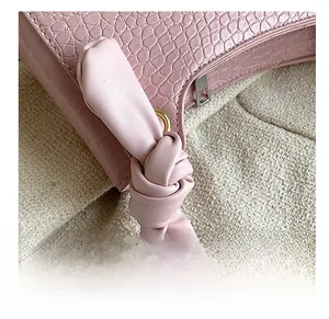 Close-up of pink faux crocodile leather bag featuring knotted strap and gold hardware