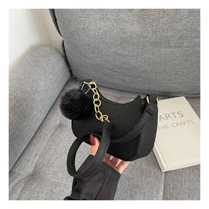 Detalle de bolso medialuna negro acolchado con cadena dorada y pompón de piel