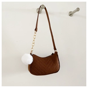 Detalle de bolso bandolera marrón con costuras en V, cadena dorada y pompón blanco