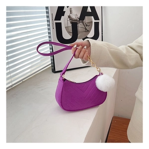 Detalle de bolso medialuna de terciopelo morado con costuras en V y pompón blanco