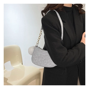 Detalle del bolso de hombro de fieltro gris con cadena dorada y pompón de peluche
