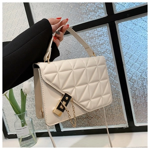 Detail of cream quilted crossbody bag featuring a gold chain and metallic lock closure