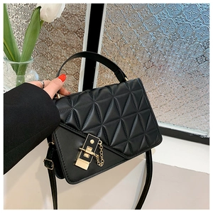 Detail of black quilted crossbody bag with gold square lock and chain on a window sill