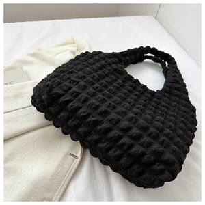 Detail view of black bubble textured tote bag on a minimalist white fabric background