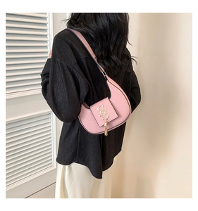 Pink crescent shoulder bag featuring gold buckle and tassel detail on black textured top