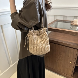 Sac seau plissé beige élégant avec cordon de serrage porté par une femme à l'intérieur