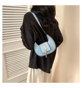 Close-up of light blue crescent bag featuring gold SS logo and tassel on a female model