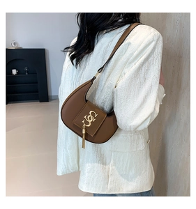 Detail view of a brown crescent hobo bag with gold logo worn over a white blazer