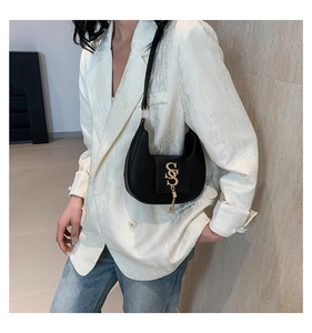 Detail of black hobo bag with golden S-shaped buckle and tassel on white blazer