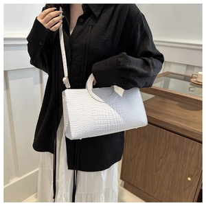 Detail of white crocodile-textured handbag featuring a semi-circular handle and gold feet