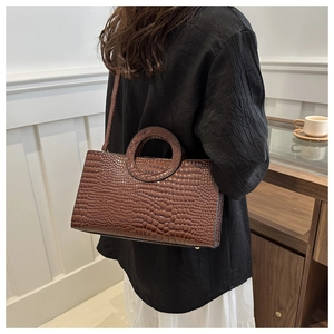 Brown crocodile-textured handbag with round top handles shown in a lifestyle setting