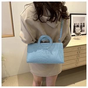 Detail of light blue crocodile pattern handbag with circular handle and crossbody strap