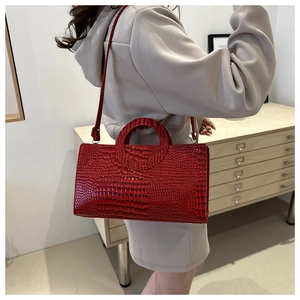 Detail of red crocodile textured rectangular handbag with round handle and shoulder strap