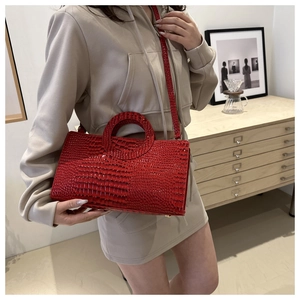 Detail of red crocodile pattern handbag with circular handle and slender shoulder strap