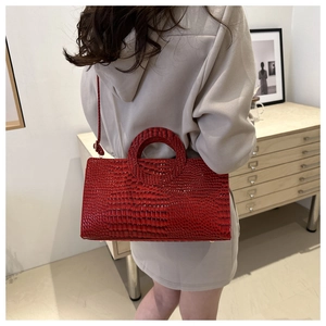 Model wearing a red crocodile embossed leather handbag with unique round cutout handle