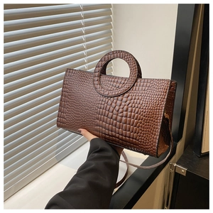 Detail of dark brown crocodile pattern handbag with unique circular cutout handle