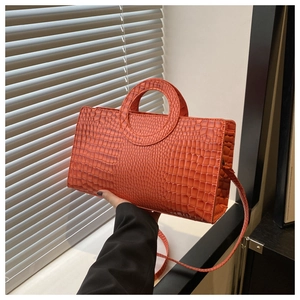 Detail of brick red crocodile pattern handbag with unique round handle and slim shoulder strap
