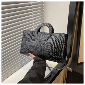Detail of glossy black faux crocodile pattern handbag with unique round handle and strap