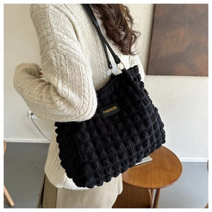 Detalle de bolso tote negro con textura de burbujas y etiqueta de moda al hombro